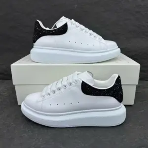 Tenis Alexander McQueen blancos de cuero con suela plataforma y detalle de brillo negro en el talón, sobre una caja blanca.