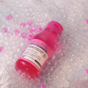 Botella de shampoo rosado de 550 ml sobre burbujas de jabón, etiqueta visible, hidratante con colágeno.