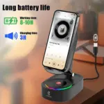 Soporte negro y base con parlante inalámbrico circular, luces LED de colores y celular instalado, conectado a un cable USB sobre escritorio de madera.
