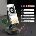 Soporte negro plegable para celular sobre base ovalada con parlante circular, luces LED de colores y panel de control lateral con puertos USB.