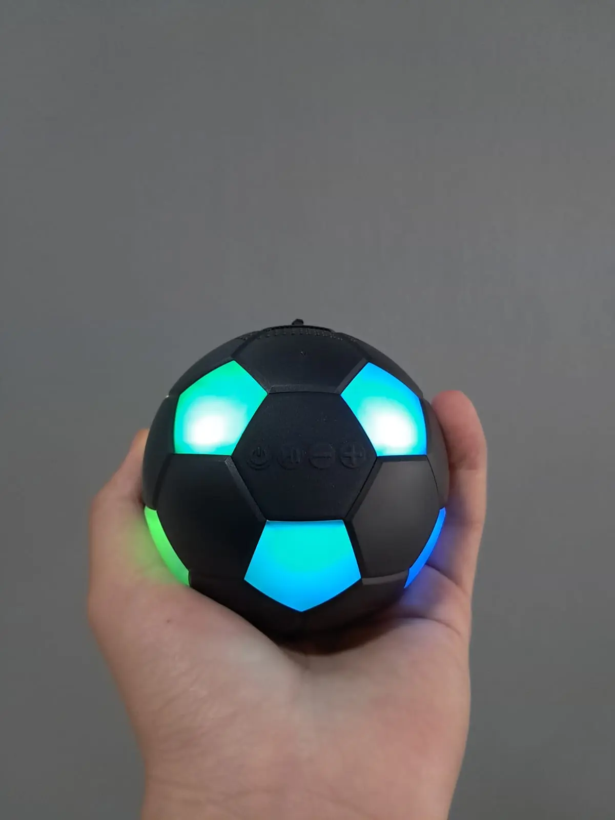 Parlante inalámbrico portátil Bluetooth en forma de balón de fútbol negro mate con luces LED brillantes y controles táctiles frontales sostenido en una mano
