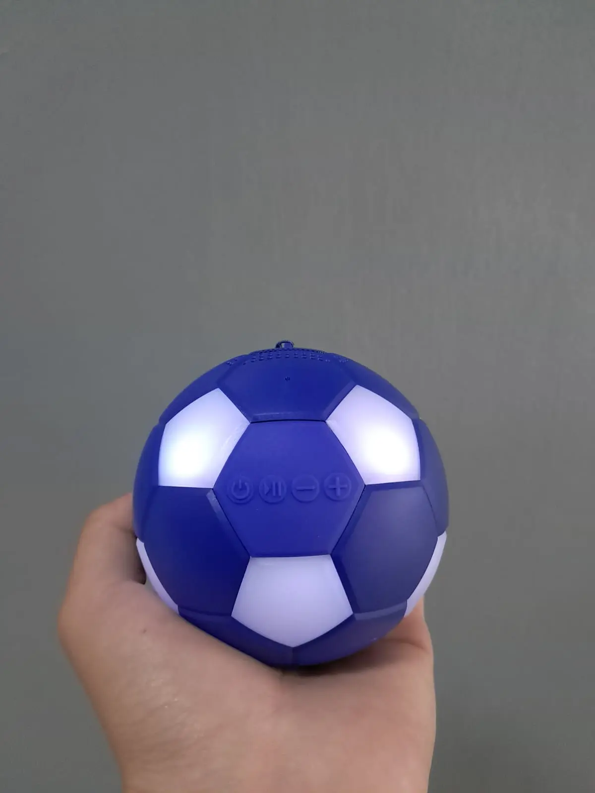 Parlante inalámbrico portátil Bluetooth en forma de balón azul con diseño de fútbol, luces LED brillantes y controles frontales, sostenido en una mano.
