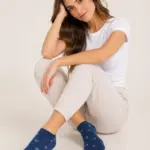Mujer sentada con medias tobilleras azules de diseño estampado y tejido suave, combinadas con camiseta blanca y pantalón cómodo.