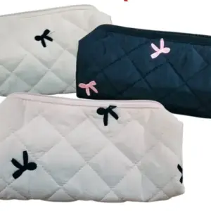 Tres cosmetiqueras acolchadas con patrón de rombos; una negra con lazos rosados y dos blancas con lazos negros, diseño portátil con cierre.