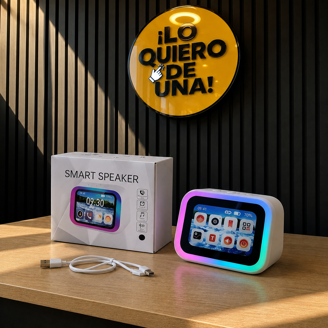 Parlante inteligente blanco con pantalla táctil, borde RGB, caja de empaque y cable USB sobre mesa de madera ante muro negro acanalado.