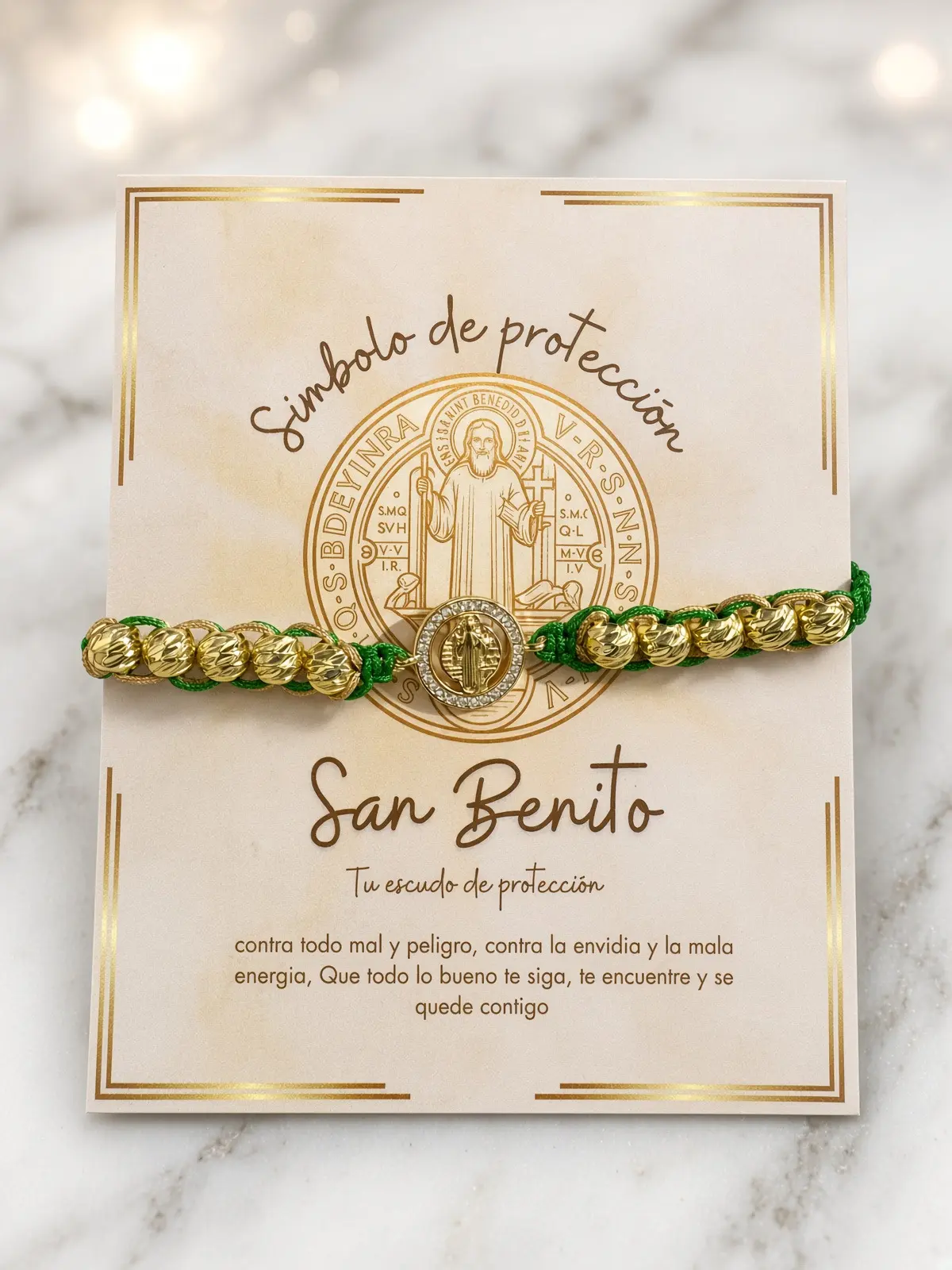 Pulsera tejida de cordón verde con cuentas doradas y medalla de San Benito sobre tarjeta con diseño de protección y fondo de mármol.
