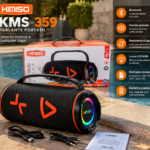 Parlante portátil bluetooth negro con luces LED RGB en los laterales, acompañado de su caja, cable de carga, cable auxiliar y manual en el borde de una piscina.