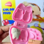 Estuche rosa con forma de diente que contiene masa blanca en un molde, parte de un kit de odontología infantil para juego de rol.