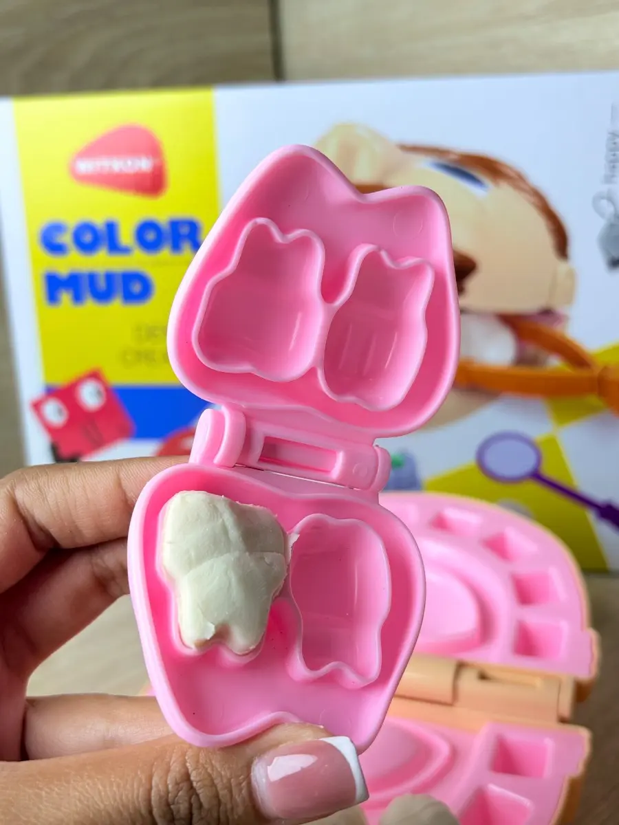 Estuche rosa con forma de diente que contiene masa blanca en un molde, parte de un kit de odontología infantil para juego de rol.