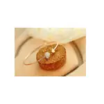 Pulsera dorada rosada con abertura y dos dijes de corazón, uno liso y otro pavé, apoyada sobre un cilindro de corcho.