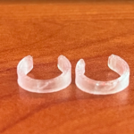 Par de correctores de orejas semitransparentes con forma de C, de plástico discreto, sobre una superficie de madera.