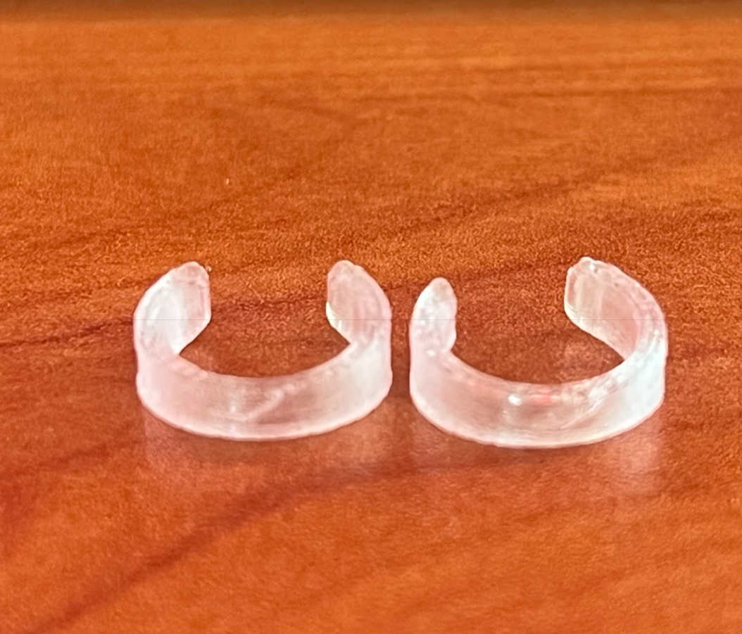 Par de correctores de orejas semitransparentes con forma de C, de plástico discreto, sobre una superficie de madera.