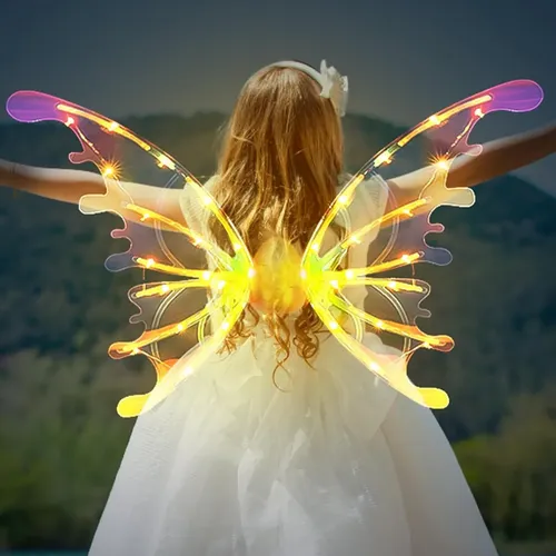 Niña con vestido blanco y alas de hada transparentes con luces LED amarillas encendidas, extendidas al aire libre frente a un paisaje montañoso.