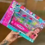 Mano sosteniendo caja diagonal de set rosado para crear manillas infantiles con hilos, dijes de corazones y cuentas coloridas.