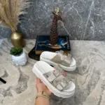 Sandalias de plataforma blanca con doble correa de brillos plateados, sostenidas por una mano en primer plano.