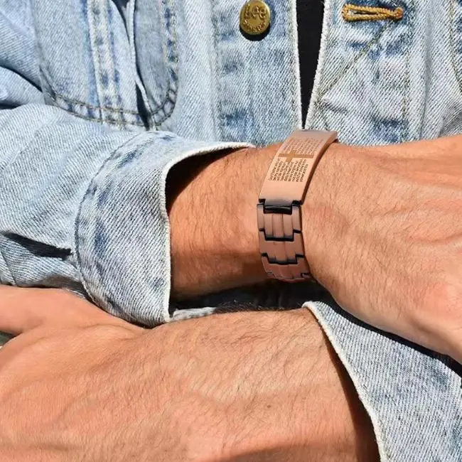 Pulsera magnética color beige con textura de eslabones y detalle de cruz, usada en la muñeca con chaqueta de mezclilla azul claro.
