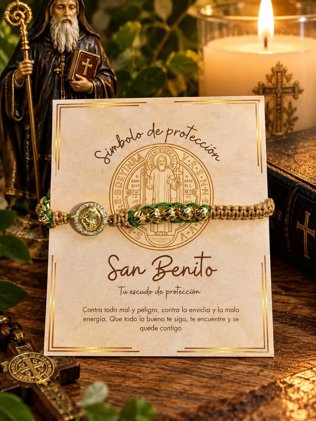 Pulsera tejida beige y verde con medalla dorada de San Benito sobre tarjeta descriptiva, vela encendida y estatuilla religiosa.