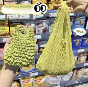 Bolsa reutilizable de tela verde arrugada, muy elástica y compacta en la mano, y expandida con gran capacidad en supermercado.