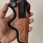 Funda para pistola en cuero ecológico marrón con bordes negros, gancho metálico de sujeción para cinturón y correa ajustable con botón a presión