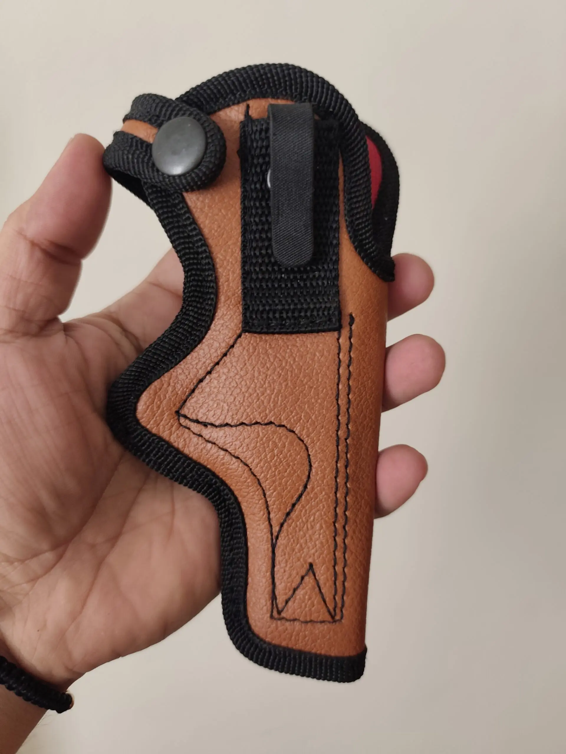 Funda para pistola en cuero ecológico marrón con bordes negros, gancho metálico de sujeción para cinturón y correa ajustable con botón a presión