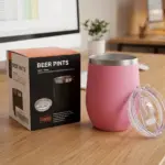 Vaso térmico rosa de acero inoxidable con tapa transparente y caja de presentación negra con la medida 360 ml sobre escritorio de madera.