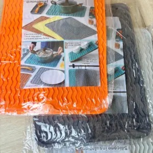 Tapete térmico de silicona naranja con textura ondulada antideslizante, apilado sobre otros protectores grises y blancos en bolsa transparente.