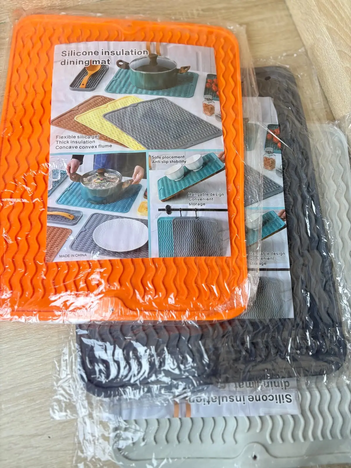 Tapete térmico de silicona naranja con textura ondulada antideslizante, apilado sobre otros protectores grises y blancos en bolsa transparente.