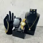 Smartwatch A58 Plus negro con correa de silicona y reloj analógico dorado con diamantes de imitación, exhibidos junto a pulsera, collar con dije y aretes dorados sobre soportes negros.