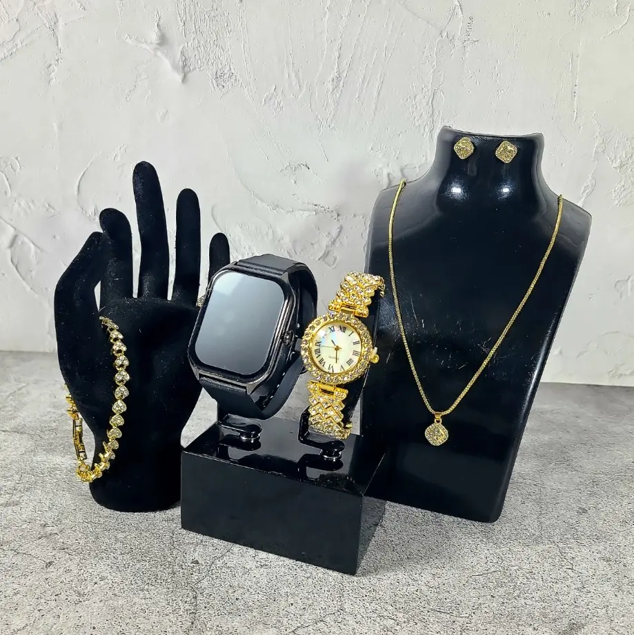 Smartwatch A58 Plus negro con correa de silicona y reloj analógico dorado con diamantes de imitación, exhibidos junto a pulsera, collar con dije y aretes dorados sobre soportes negros.