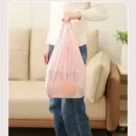 Bolsa expandible de malla color rosa con víveres adentro, sostenida por una persona frente a un sofá en la sala.