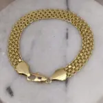 Pulsera masculina de tejido chino grueso con textura detallada en color oro y broche de langosta sobre fondo de mármol blanco.