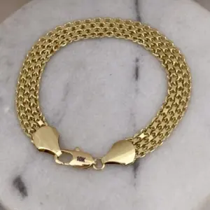 Pulsera masculina de tejido chino grueso con textura detallada en color oro y broche de langosta sobre fondo de mármol blanco.