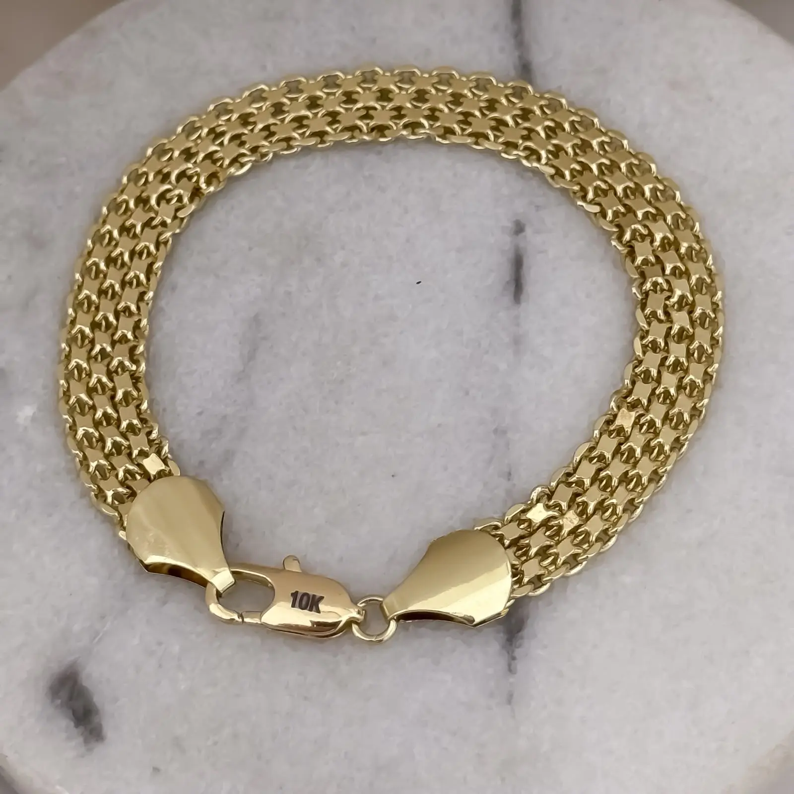 Pulsera masculina de tejido chino grueso con textura detallada en color oro y broche de langosta sobre fondo de mármol blanco.