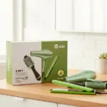 Set de cuidado capilar 3 en 1 verde aguacate con secador, plancha y cepillo redondo sobre mesa de madera junto a su caja de presentación.