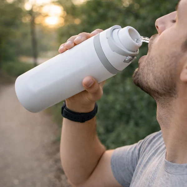 Hombre bebiendo de termo deportivo blanco de acero inoxidable con doble boquilla gris y acabado mate al aire libre.