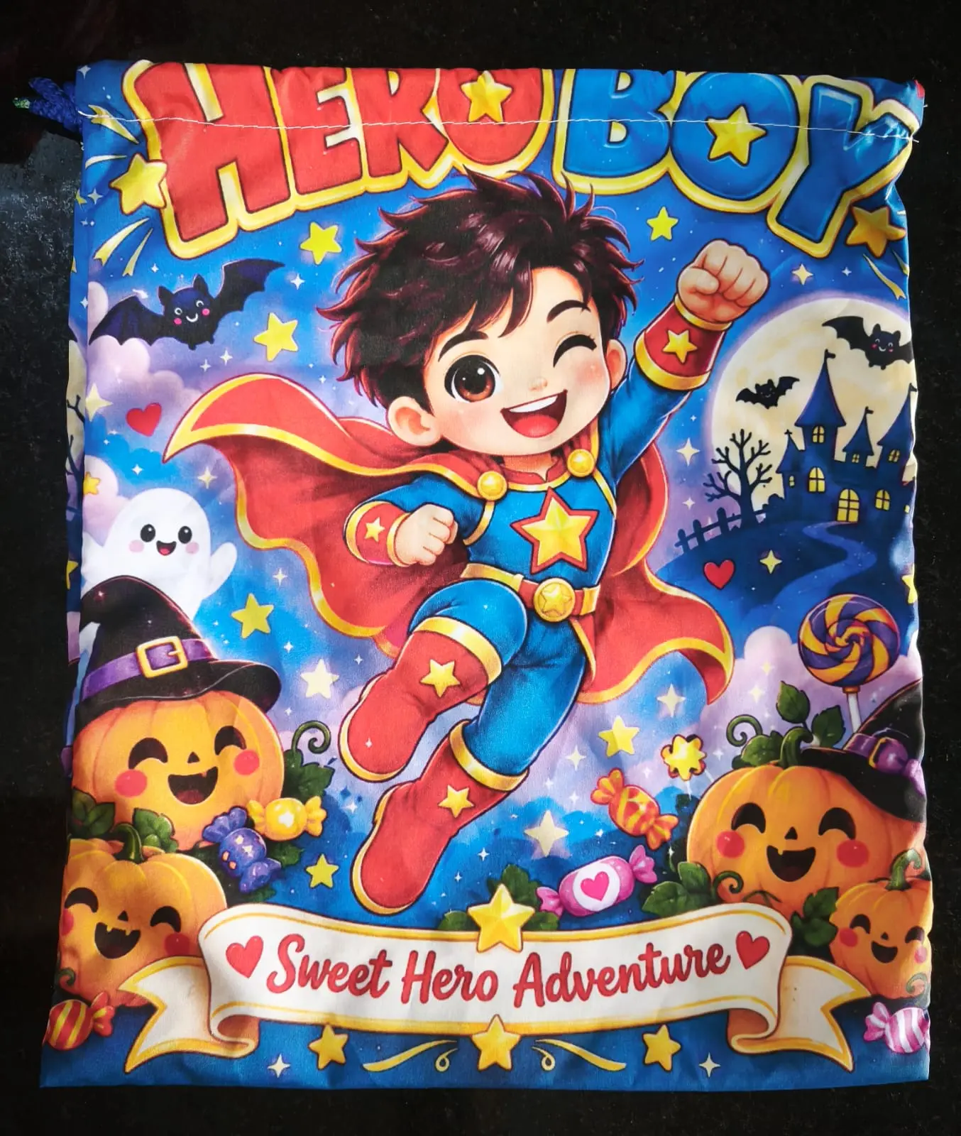 Bolsa de tela azul con cordón para Halloween, diseño de niño superhéroe volando, calabazas sonrientes y texto Sweet Hero Adventure.