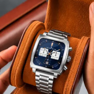 Reloj cronógrafo Leonidas con caja cuadrada y esfera azul, presentado en estuche cilíndrico de cuero gamuzado color caramelo con cierre de broche.