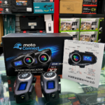 Caja negra de intercomunicador Bluetooth Q58-Max para casco con dos unidades principales, manual ilustrado y estante de tienda de fondo.