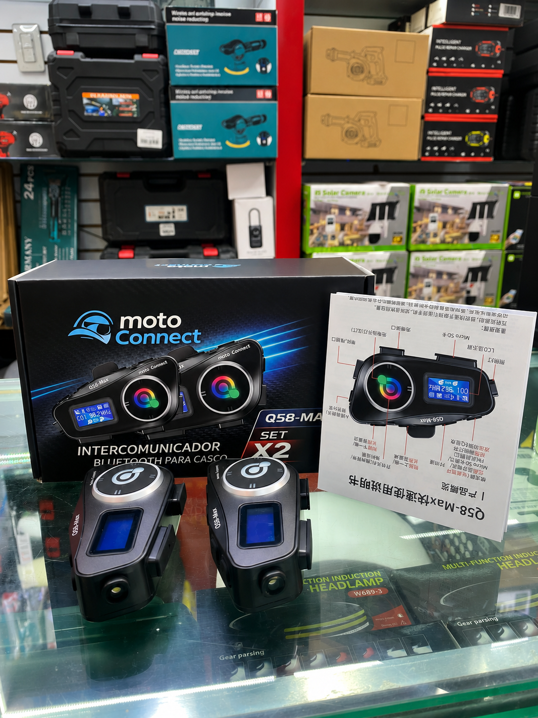 Caja negra de intercomunicador Bluetooth Q58-Max para casco con dos unidades principales, manual ilustrado y estante de tienda de fondo.
