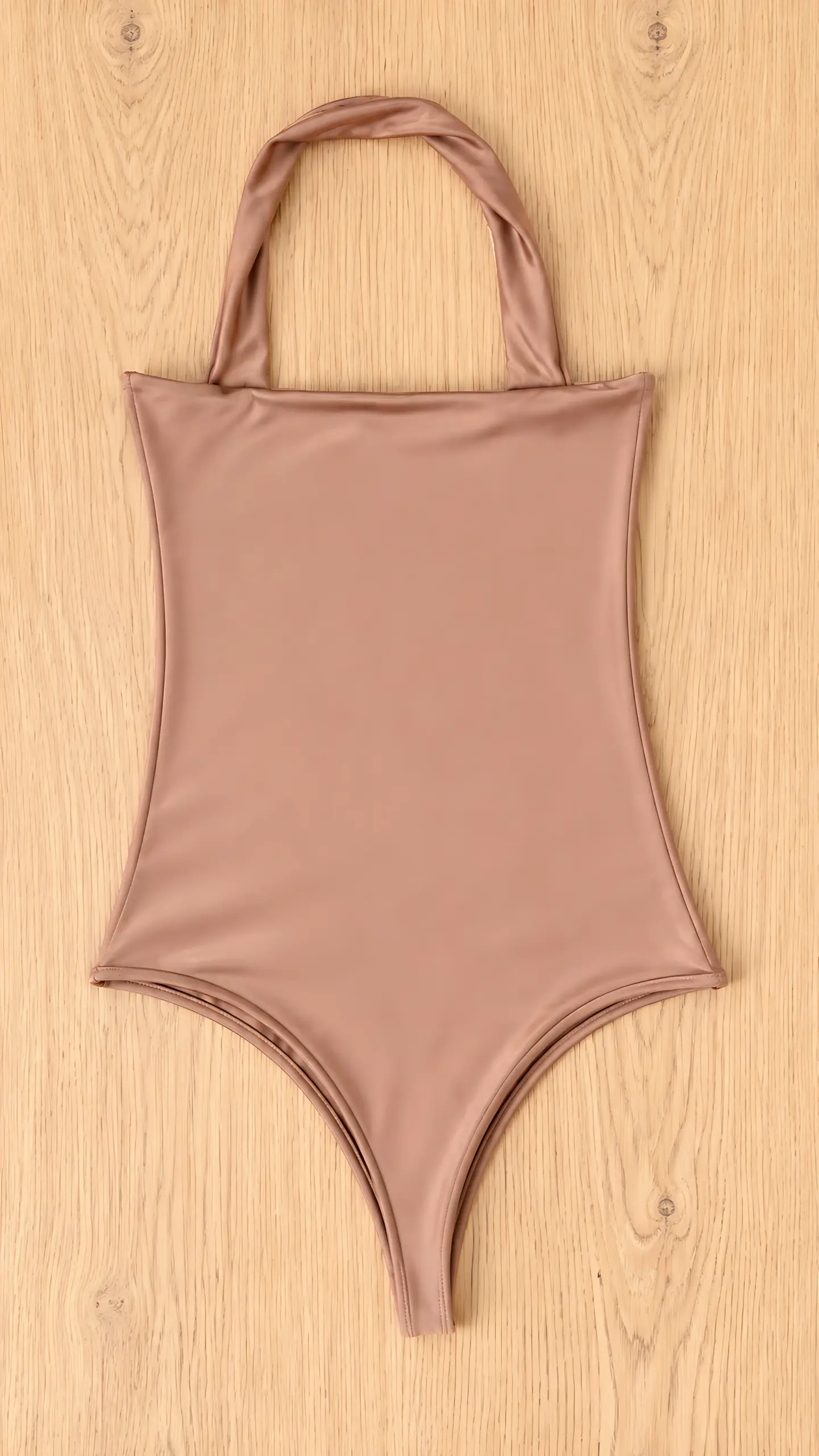 Body color café con cuello halter y corte alto en las piernas, de tela suave y elástica, sobre fondo de madera clara.