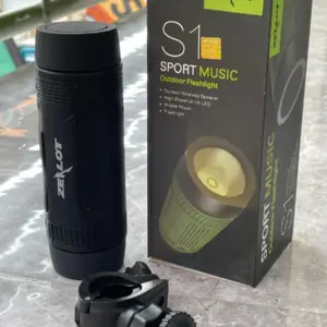 Parlante Bluetooth Zealot S1 negro cilíndrico, caja de empaque verde y negra y soporte de montaje sobre superficie de mármol.
