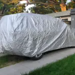Carpa para carro color plata metalizada cubriendo un vehículo estacionado en una entrada, con textura brillante y protectora.