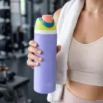 Mujer sosteniendo termo deportivo morado de acero inoxidable de 710 ml con tapa verde y boquilla rosada en el gimnasio