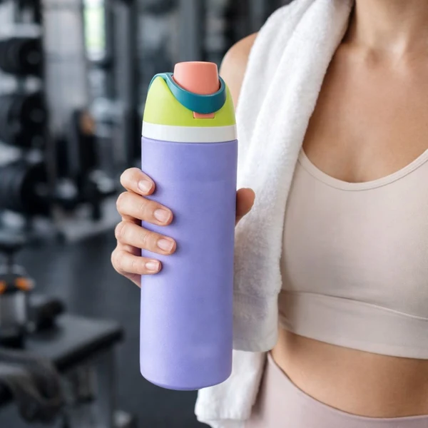Mujer sosteniendo termo deportivo morado de acero inoxidable de 710 ml con tapa verde y boquilla rosada en el gimnasio