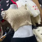 Camisa tejida sin mangas color café con diseño de trenzas y cuello en V, mostrada de perfil en un maniquí blanco.