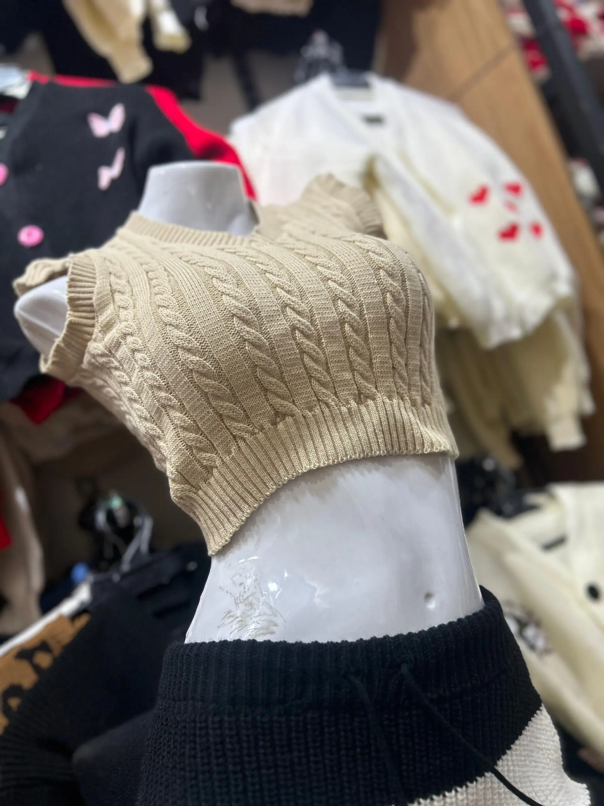 Camisa tejida sin mangas color café con diseño de trenzas y cuello en V, mostrada de perfil en un maniquí blanco.