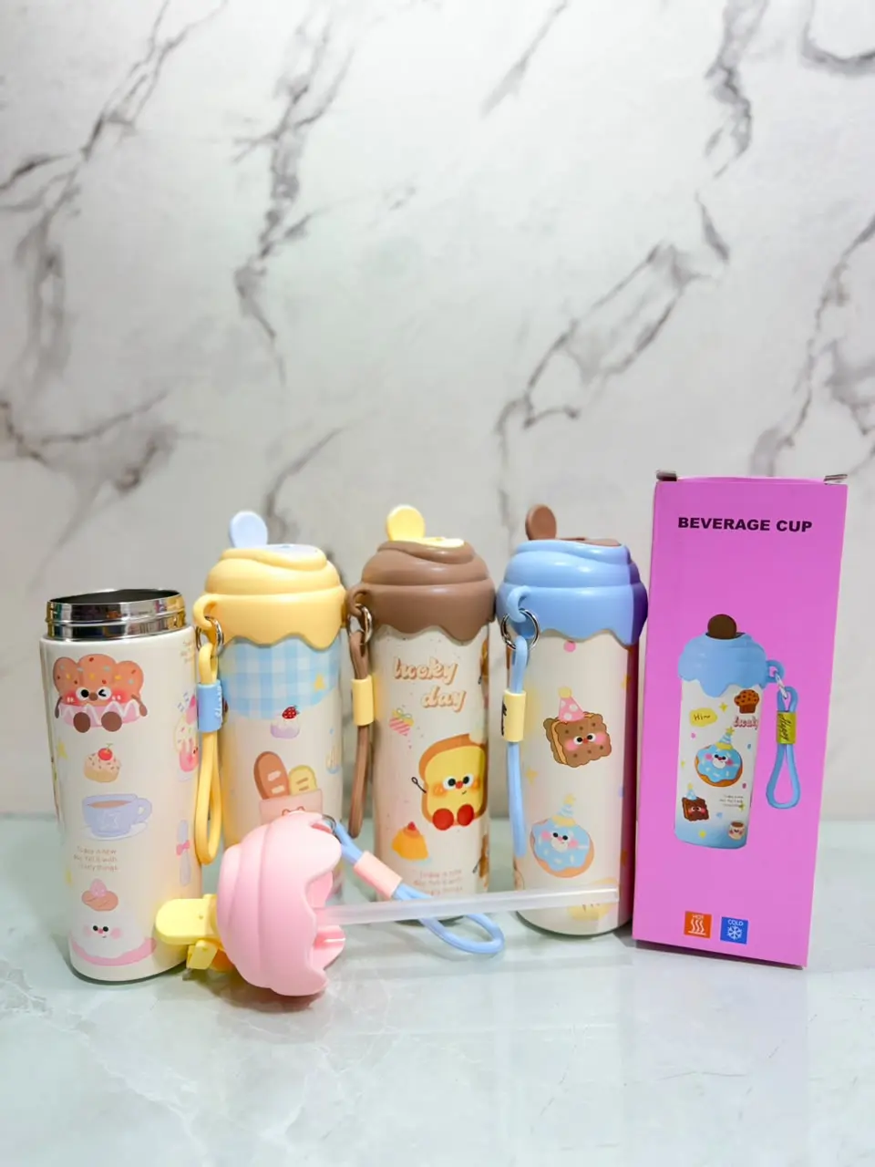Cuatro termos cilíndricos de acero con diseños kawaii de postres, uno abierto con pitillo y su caja rosa de empaque.