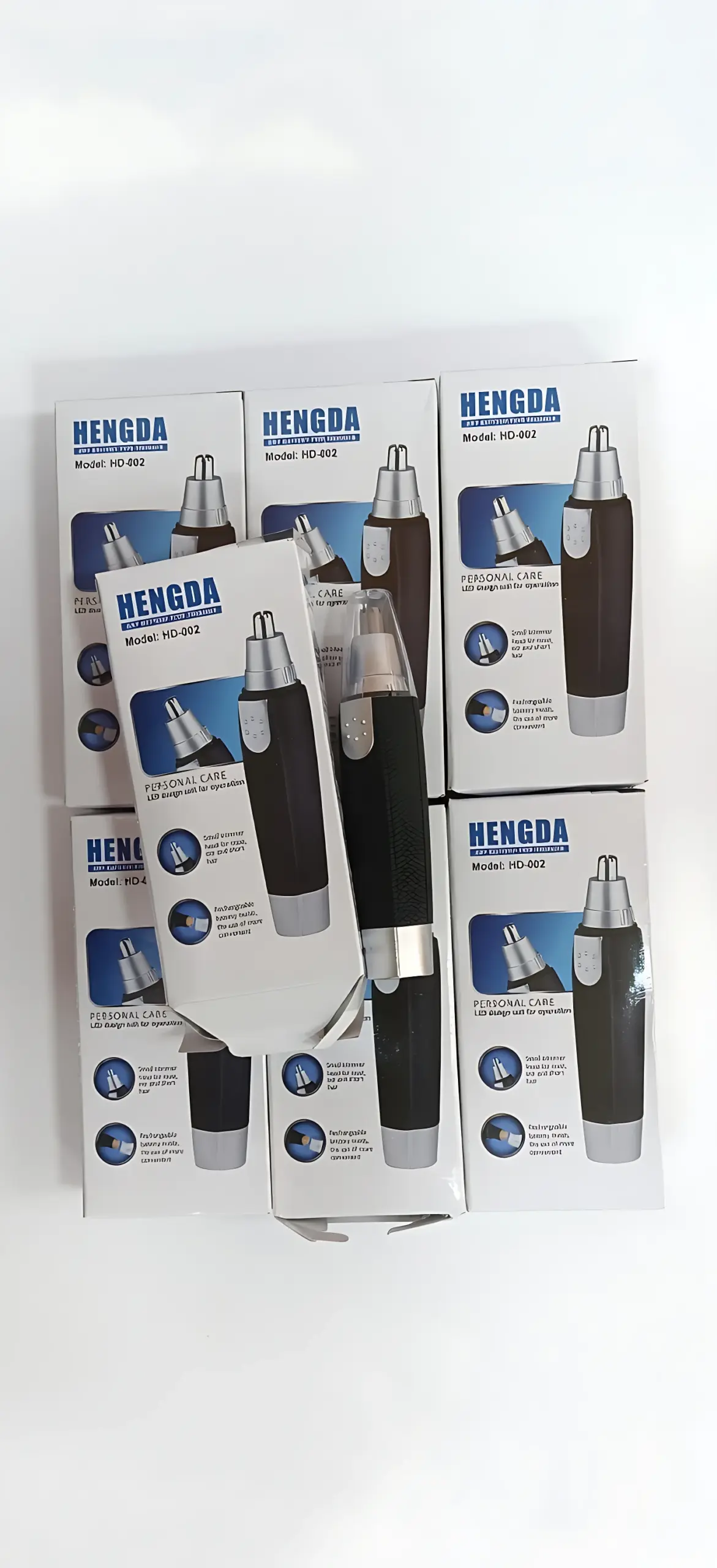 Seis cajas de depilador nasal Hengda modelo HD-002 en negro y plateado, con un aparato fuera de su empaque mostrando el cabezal de corte metálico.