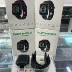 Smartwatch deportivo negro con monitor de frecuencia cardíaca, cuatro cajas apiladas de fondo y unidad con correa en estuche plástico.