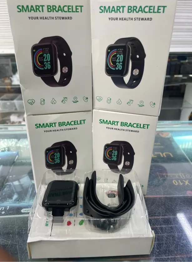 Smartwatch deportivo negro con monitor de frecuencia cardíaca, cuatro cajas apiladas de fondo y unidad con correa en estuche plástico.
